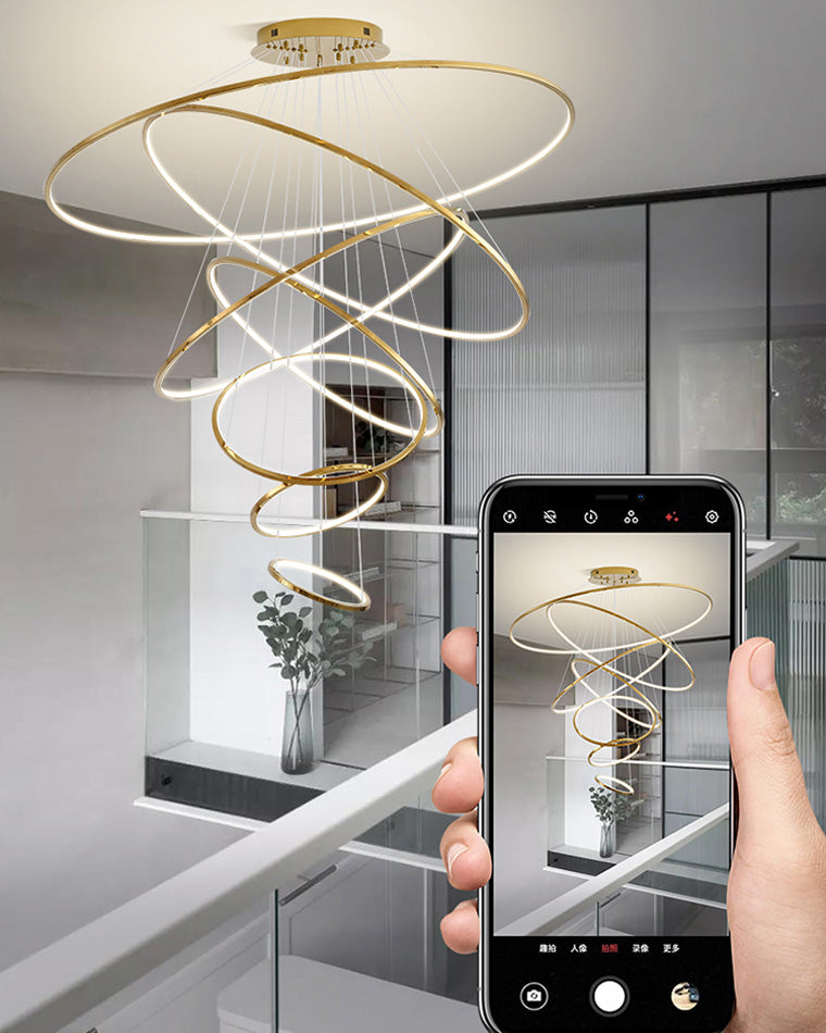 Golden LED chandelier viewed from an upper landing, revealing how the long cascading form connects multiple floors with one dramatic focal point.