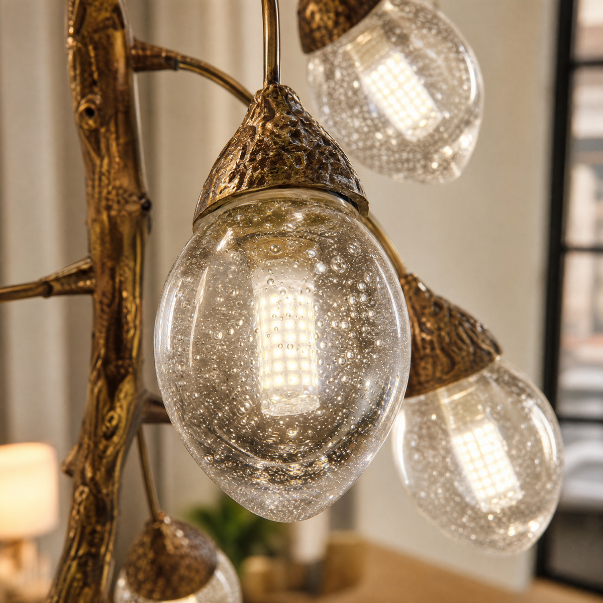 A modern chandelier with an antique brass metal vine frame and glowing glass buds hanging in a bright room.
