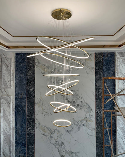 Fully illuminated gold ring chandelier against a marble feature wall, creating a luxurious centerpiece during the final installation stage.