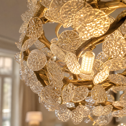 A circular gold metal chandelier with frosted glass leaf accents suspended by thin cables.
