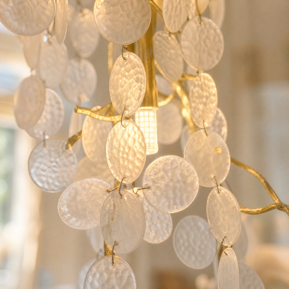 A multi-tiered cascading crystal chandelier with a gold frame hangs in a grand foyer with a curved staircase.