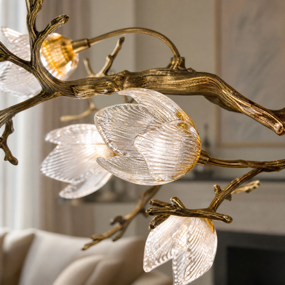 An antique brass chandelier with metal tree branches and frosted glass magnolia blossom shades suspended by multiple cables.