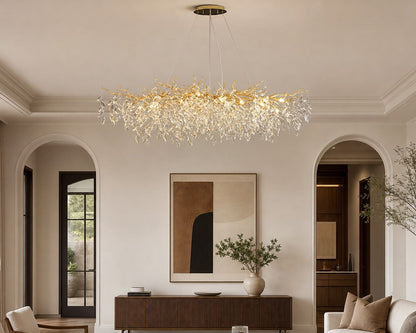 A modern crystal chandelier with a gold-toned branch-like frame hangs in a bright, elegant living room with cream walls, arched doorways, a sofa, and a dark wood coffee table.